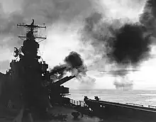 Large naval guns firing on board a ship cast in silhouette