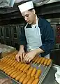 A sailor aboard the USS George Washington places corn dogs on a tray to be baked in the galley.