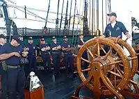 U.S. Navy personnel aboard USS Constitution, by the ship's wheel