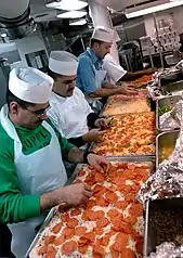 Toppings being placed on pan pizzas