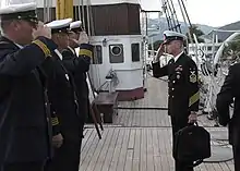 A colour photograph of naval personnel saluting each other on a sailing ship