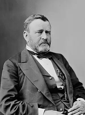 Man with light beard sitting down in suit with vest and bow tie