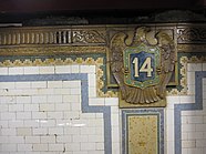 A beige, green, and blue cartouche on the wall of the station with the number "14" in white text