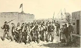 A lithograph of a large column of soldiers without weapons in disorderly dress marching outside a large stone fort being guarded by a few soldiers in dark uniforms holding rifles