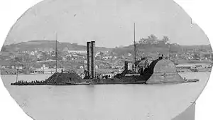 Armored steamboat in front of bluffs with buildings