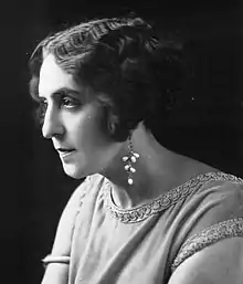 A white woman in near-profile, with wavy cropped hair, wearing beaded drop earrings.