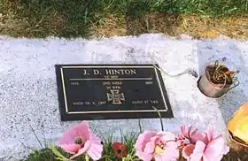  A bronze plaque headstone set in a block of concrete amongst grass, with flowers in the foreground.