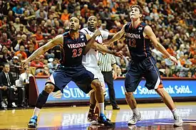 A college basketball player dressed in white with orange and blue bordering prepares to shoot a free throw.