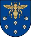 A coat of arms depicting a golden scarab with wings and legs outstretched flying over six purple flowers all on a blue background