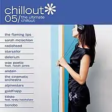 A woman wearing in black is grabbing the white column in front of her with both hands with a pair of headphones on; above her, the title of the album is visible on a blue background in a white font.