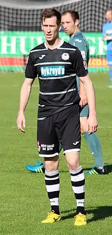 A footballer wearing a black football kit with white horizontal stripes