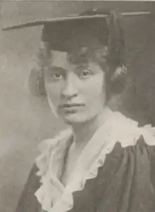 A young white woman wearing a mortarboard cap and academic robe with a white ruffled collar