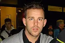 A brown-haired young man looks into the camera.