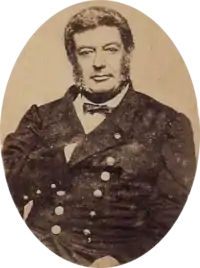 Photographic portrait of a dark-haired man with sideburns, dressed in a double-breasted military tunic with his right hand tucked under the lapel of his jacket