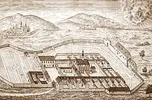 Engraving showing a Carthusian monastery situated at the foot of hills and surrounded by a wall.