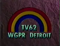 On a dark purple textured background, a rainbow consisting of three colors—blue, yellow, and red, from inside to outside. Beneath the rainbow is the text "TV62 / WGPR DETROIT" in a light green.