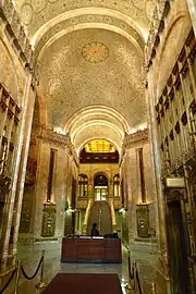 Photograph showing part of the lobby with an ornate ceiling and a staircase in the background