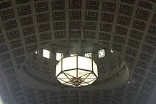 The coffered ceiling of the banking room, with a chandelier hanging from it. The dome in the ceiling is visible in the background.