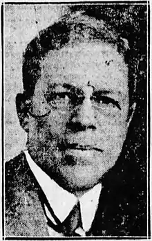 Black and white photo of a middle-aged man wearing eyeglasses, and a white high-collar dress shirt