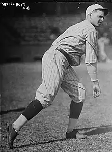 A man wearing a pinstriped baseball uniform stands truned–his left having just thrown a baseball.