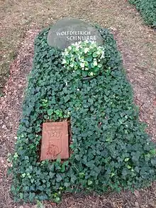 A grave covered in plants. The inscription on the headstone reads "WOLFDIETRICH SCHNURRE".