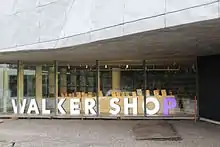 Window of a modern store, large lighted letters spelling Walker Shop in white, with the P in purple