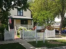 Pale yellow wooden house with brown trim surrounded by white picket fence