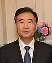 a man with a wavy haircut, wearing a white shirt, a suit and a blue tie
