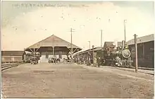 A postcard view of a train station with tracks on both sides