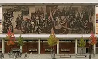 A mural consisting of red and black figures painted on concrete, depicting the history of the struggle of workers in East Germany