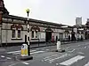 A dirty, white-bricked building with a rectangular, dark blue sign reading "WESTBOURNE PARK STATION" in white letters all under a blue sky