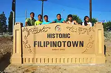 Photograph of a sign located in Los Angeles with people standing behind it that reads Historic Filipinotown