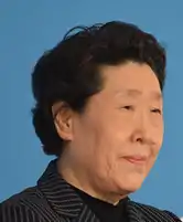 Portrait photograph of Whang Youn Dai (woman) at 76-77 years old. She has short black hair and wears a formal striped jacket.