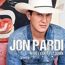 A man wearing a denim shirt and white cowboy hat is sitting on a red wooden bench.