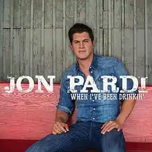 A man wearing a blue denim shirt and jeans is sitting on a red wooden bench.