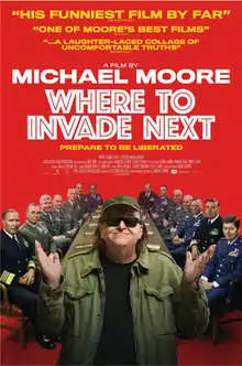 Michael Moore facing towards a viewer with a group of generals sitting on a conference table behind Moore.