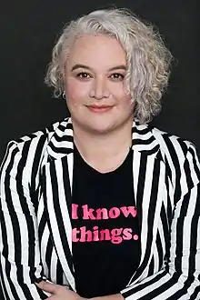 Whiti smiles at the camera, a women with curly hair and a striped jacket.