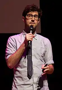 A man wearing a tie speaking into a microphone and holding a slide projector