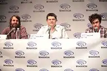 Three men sit at a table at a convention.