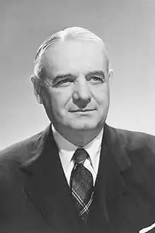 Head and shoulders of an older man with neatly combed and parted gray hair wearing a suit and tie.