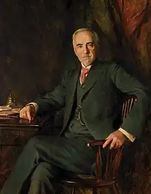 portrait of a man in his sixties or seventies wearing a suit seated at a desk