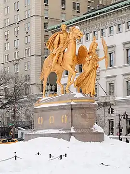 A gold statue of a man riding a horse and a winged-person walking beside the horse