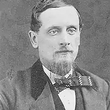 Shoulder high portrait of middle aged man with dark hair wearing Chesterfield styled jacket, bow tie and white shirt