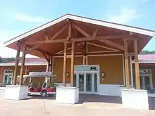 A large wooden building with a red roof, three wooden posts, with an electric golf cart parked in front.