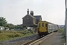 A diesel train with an old station building in the background