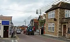 Street scene with houses and shops on both side of road on which there is a tractor.