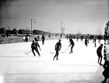 Black and white photo of young men playing ice hockey on an outdoor rink, circa 1923