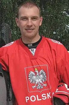 A young man wears the Polish national ice hockey team jersey while posing casually outside for a photo.