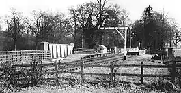 Short wooden platform on top of a bridge. A small wooden hut in the background is the only visible building.