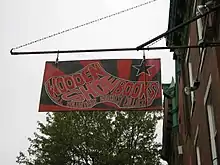 a red and black sign hanging from a building with an image of a shoe and text reading "Wooden Shoe Books: all volunteer anarchist collective"